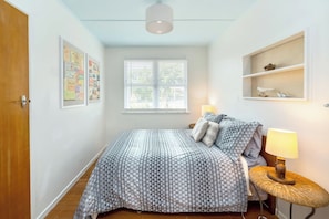 A bedroom with a bed, a bedside lamp, a window, and a wall-mounted shelf.