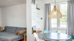 Una sala de estar moderna con un sofá gris, una mesa de comedor con sillas y una lámpara colgante.