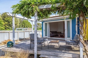 A covered outdoor seating area with a pergola, a sliding glass door leading to a room with a couch and a table, and a wooden deck.