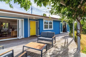 A blue house with a wooden deck, a yellow door, and a grey sofa.
