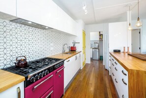 A modern kitchen with a gas stove, pink oven, and wooden countertops. - Little Blue Bach, Martinborough (Martinborough)