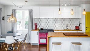Una cocina moderna con armarios blancos, horno rosa y salpicadero hexagonal.