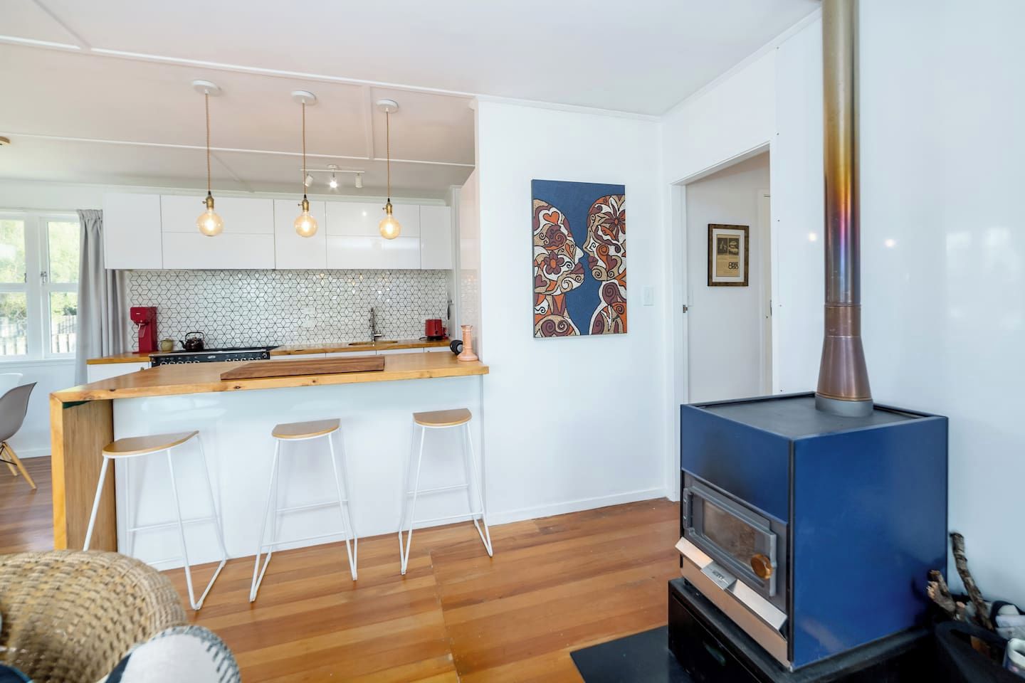 A modern kitchen with a wooden island, pendant lights, and a blue wood-burning stove.