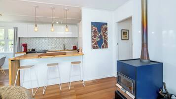 A modern kitchen with a wooden island, pendant lights, and a blue wood-burning stove.