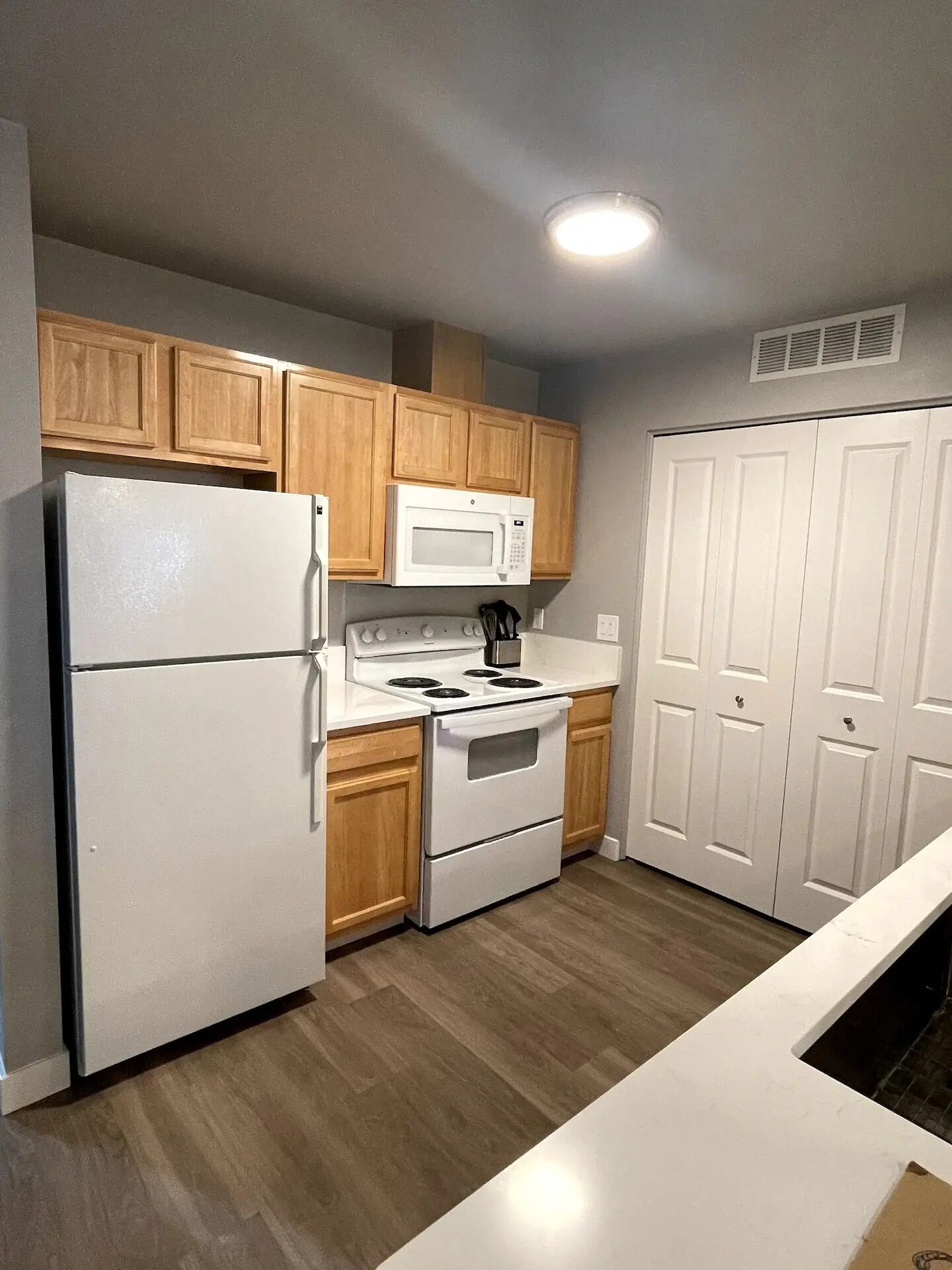 A compact kitchen with wooden cabinets, a white refrigerator, a microwave, and an oven.