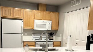 A modern kitchen with wooden cabinets, a white refrigerator, a microwave, a stove, and a sink. There are two black stools at the counter. - Renovated and Comfortable-South Meridian

 (Meridian)