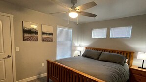 A bedroom with a wooden bed, a ceiling fan, two windows with blinds, and two wall-mounted picture frames. - Renovated and Comfortable-South Meridian

 (Meridian)