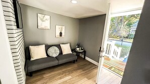 Uma sala de estar moderna com um sofá cinza, duas almofadas e uma mesinha de apoio com uma planta.