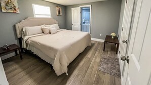 Quarto com cama grande, mesa de cabeceira, porta e pequena mesa com um vaso.