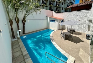 A swimming pool with a tiled deck, palm trees, and a table with chairs. - KYROS POUSADA (Maceió)