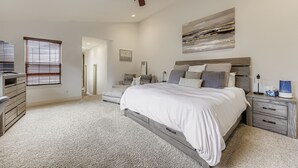 Ein Schlafzimmer mit Bett, Nachttischen, Deckenventilator, einem großen abstrakten Gemälde und einem begehbaren Kleiderschrank.