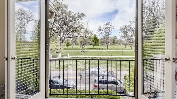 Ein Zimmer mit einer großen Schiebeglasdoor, die auf einen Balkon mit Blick auf eine Straße und Bäume führt.