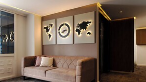 Une chambre d’hôtel moderne avec un canapé beige, une œuvre d’art représentant une carte du monde accrochée au mur et un rideau foncé.