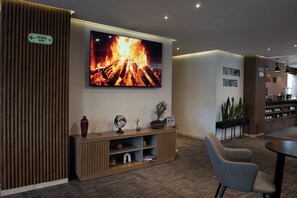 Un hall d’hôtel doté d’un téléviseur à écran plat diffusant une image de feu de cheminée, d’un comptoir de réception, d’un espace salon et d’un panneau indiquant la sortie.