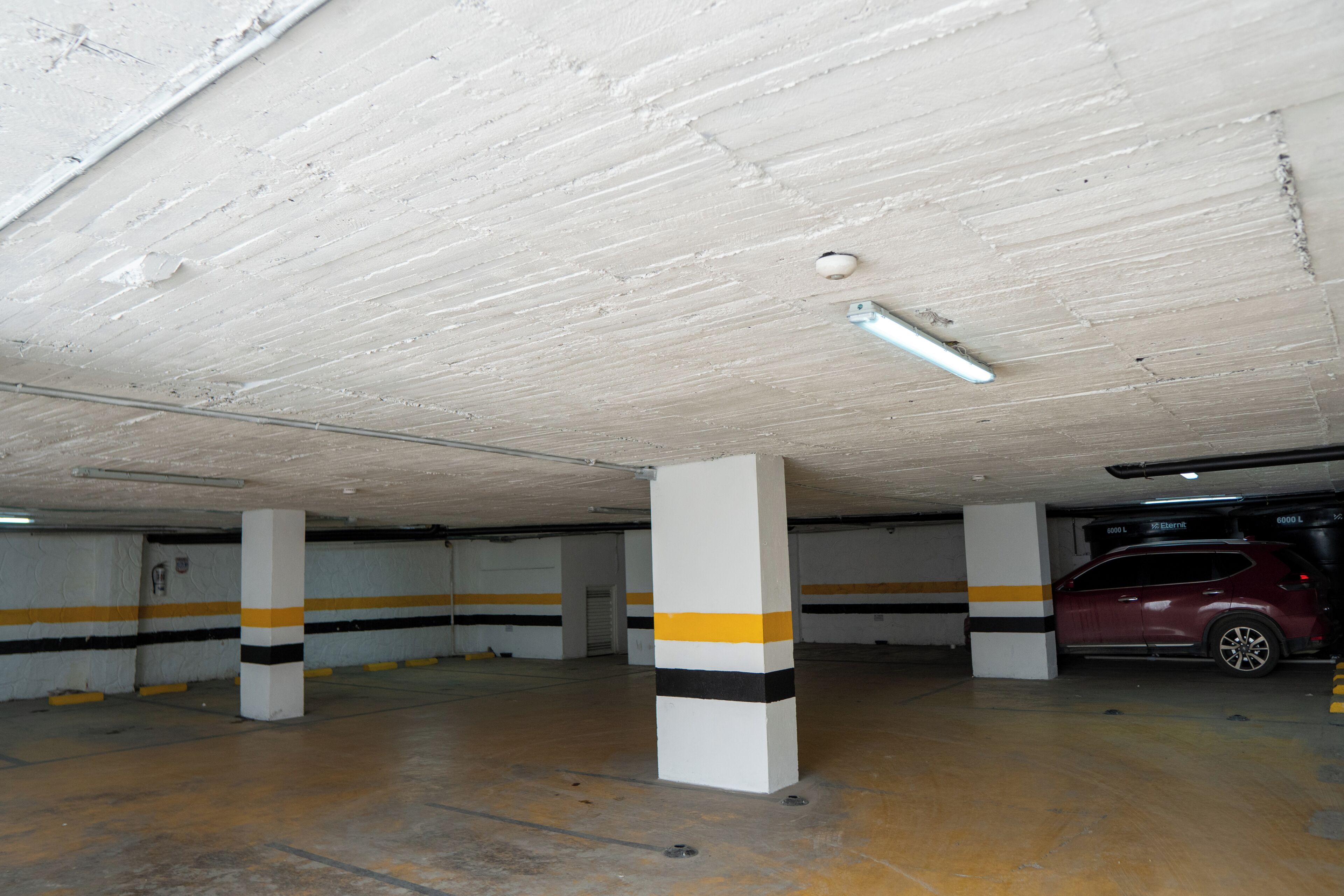 Un estacionamiento con pilares blancos, franjas amarillas y negras en las paredes, y un coche rojo estacionado en uno de los espacios.
