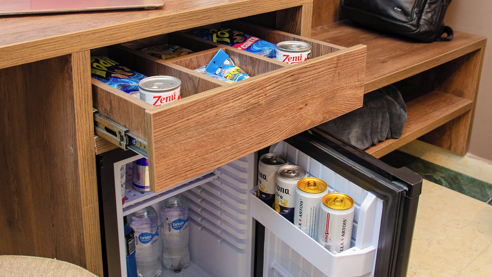 Uma gaveta de madeira com petiscos e uma lata de cerveja, e um mini-refrigerador com água engarrafada e latas de cerveja.