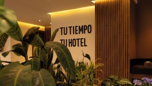 Un hall d’hôtel moderne avec un comptoir d’accueil, des plantes en pot et une enseigne sur laquelle on peut lire : « TU TIEMPO TU HOTEL ».
