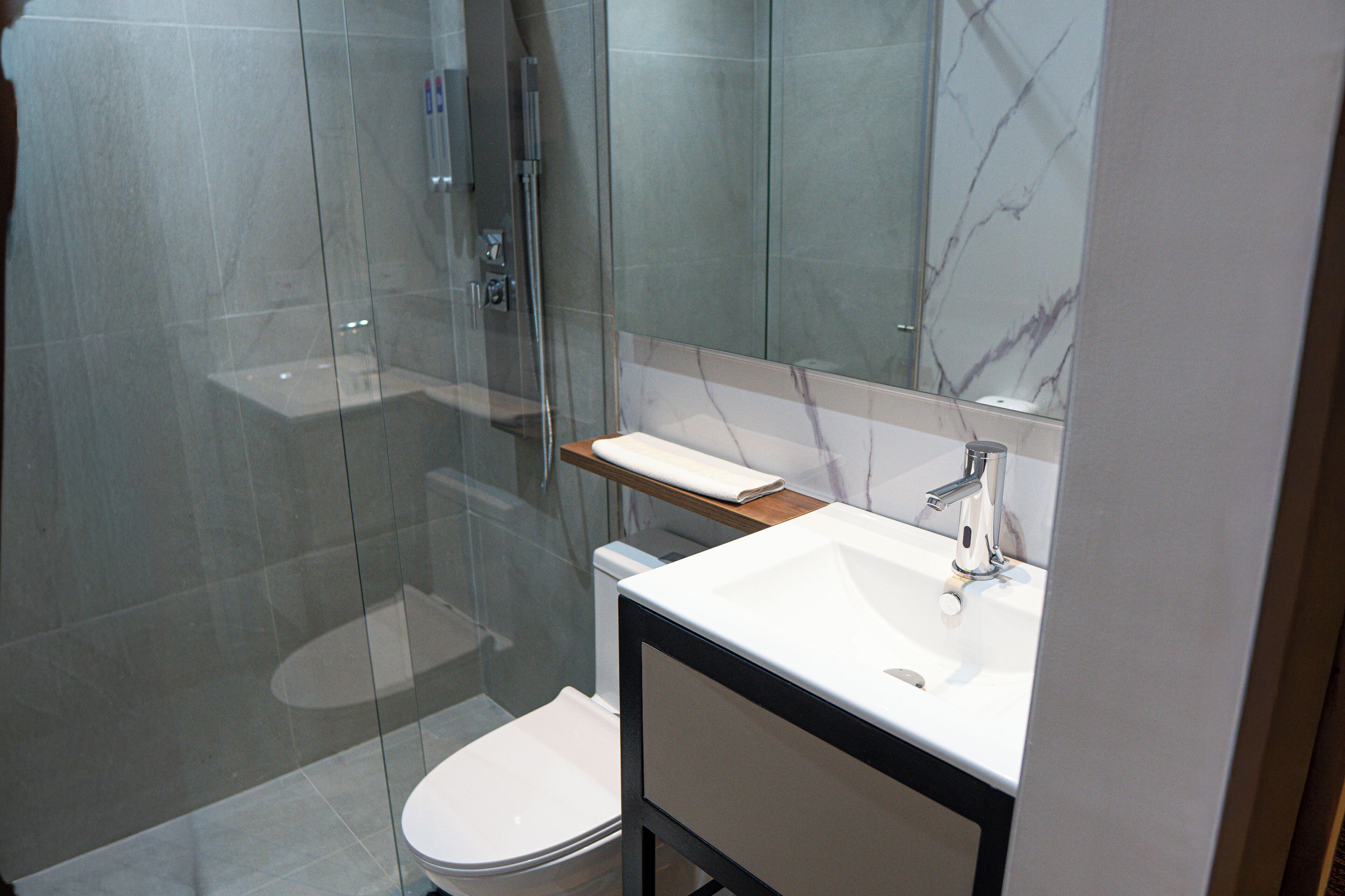 Une salle de bain moderne avec une douche à parois de verre, des toilettes blanches et un meuble-lavabo avec un miroir.