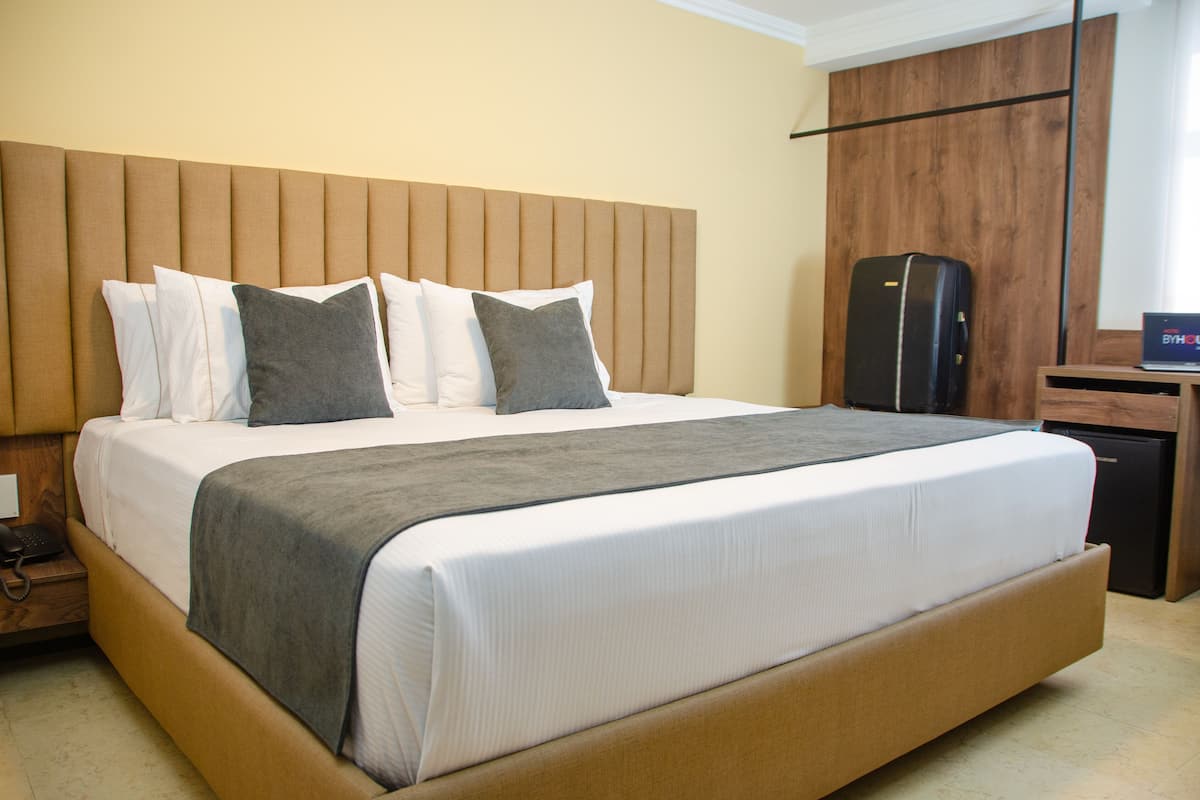 Ein Hotelzimmer mit einem großen Bett, einem hölzernen Kopfteil, einem Nachttisch mit Telefon und einem kleinen Schreibtisch mit Laptop.