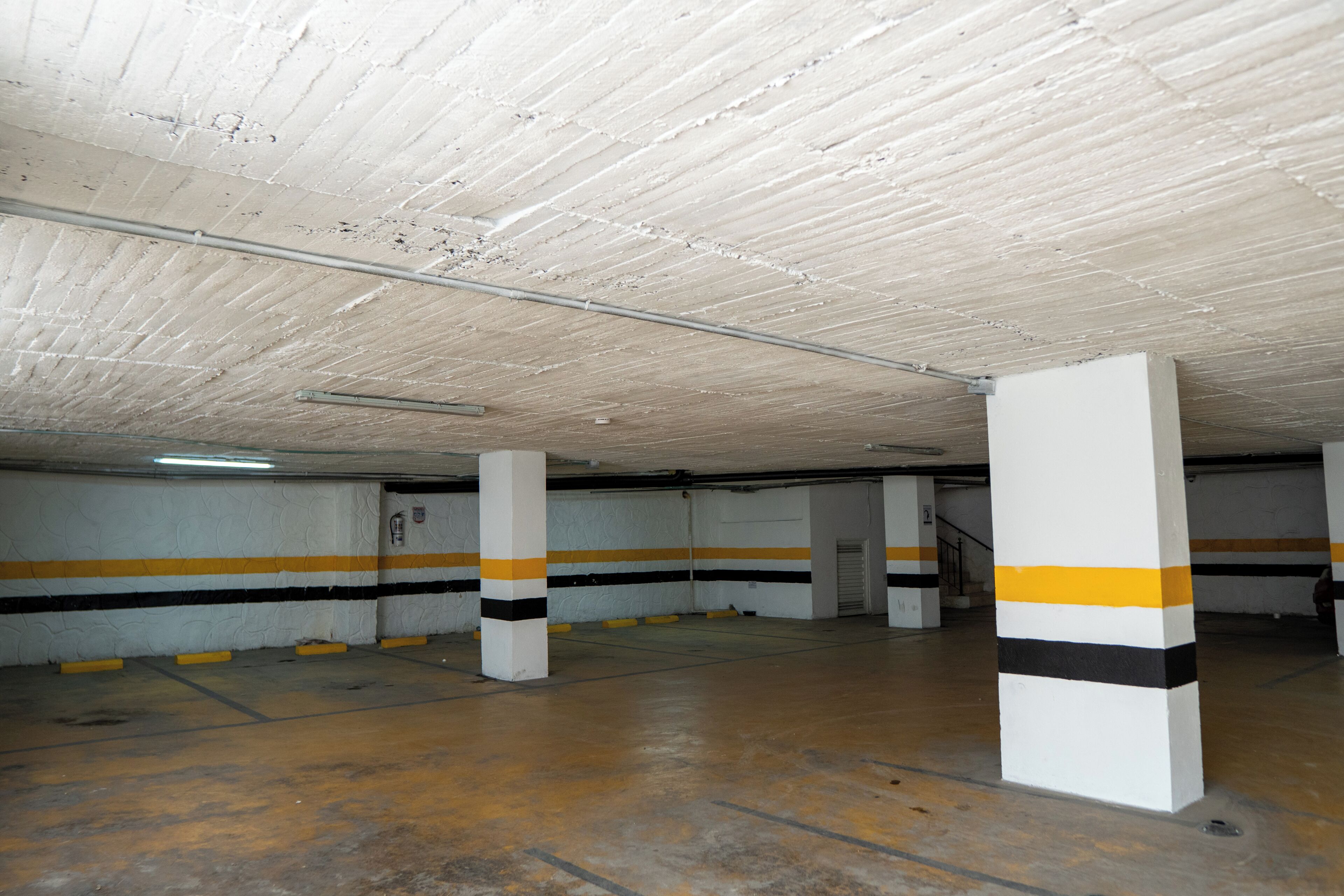 Un estacionamiento con pilares de concreto, paredes a rayas amarillas y negras y un techo texturizado.
