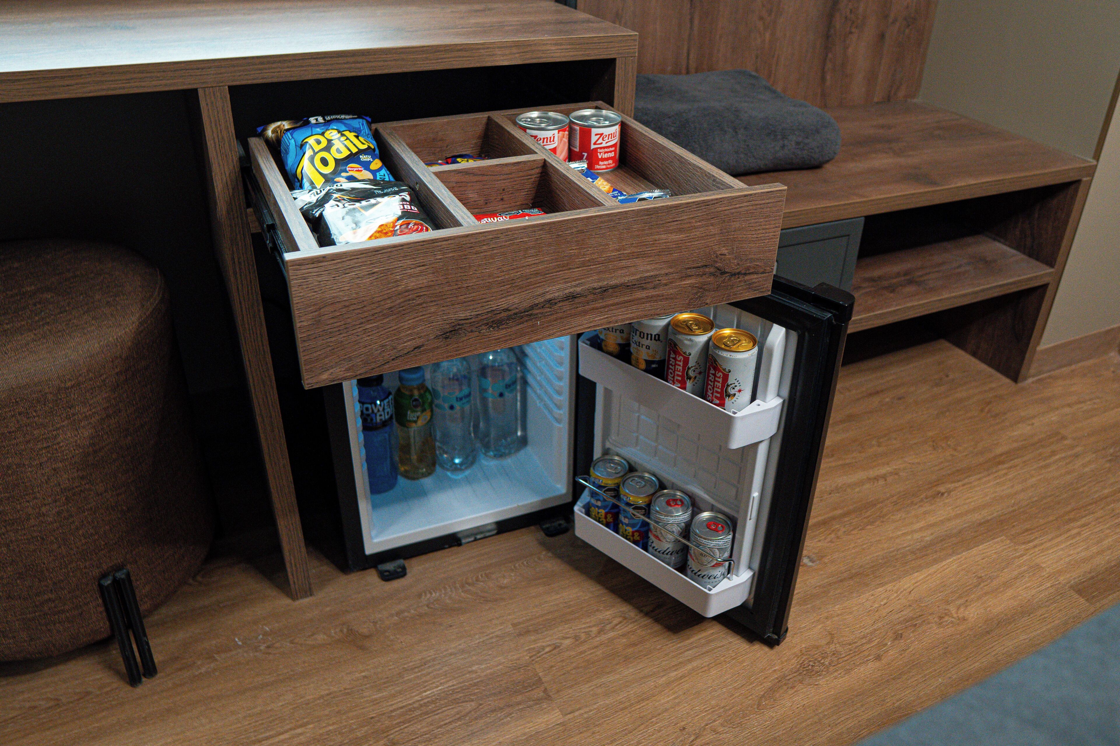 Una kitchenette compacta con un refrigerador empotrado y un mueble con aperitivos y bebidas.