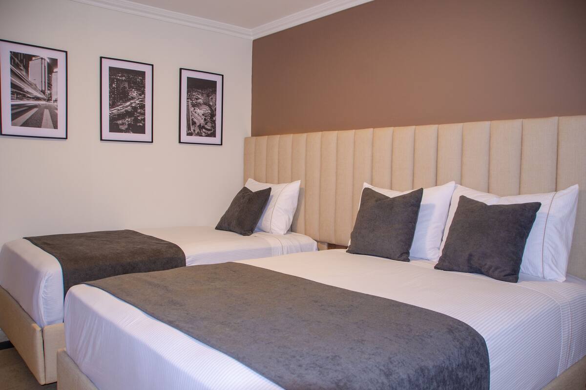 Ein Hotelzimmer mit zwei Betten, einem Kopfteil und drei gerahmten Bildern an der Wand.