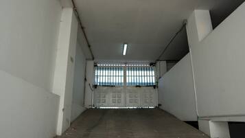 Un pasillo con entrada protegida por barrotes, paredes de concreto y una lámpara fluorescente.