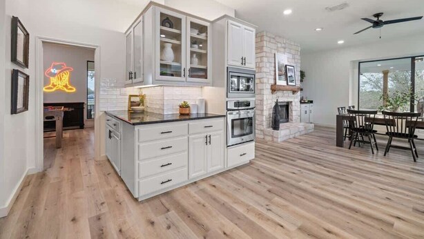 A modern kitchen with white cabinetry, a built-in oven, and a stone fireplace. - Ranch Retreat: Amenities Galore! (Leander)