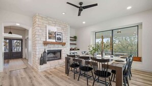 A modern living room with a stone fireplace, dining area, and large windows. - Ranch Retreat: Amenities Galore! (Leander)