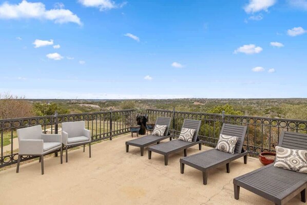 A balcony with outdoor seating, including chairs and lounge chairs, with a view of the landscape. - Ranch Retreat: Amenities Galore! (Leander)