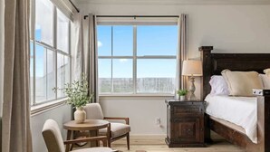 A bedroom with a large window, a bed, a nightstand, a chair, and a small table. - Ranch Retreat: Amenities Galore! (Leander)