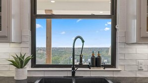 A kitchen with a black sink, a window with a view of a cityscape, and a potted plant on the counter. - Ranch Retreat: Amenities Galore! (Leander)