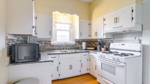 A compact kitchen with white cabinets, a stove, a microwave, and a window with blinds. - Walk to Parks & Dining! Memphis Home w/ Yard (Memphis)
