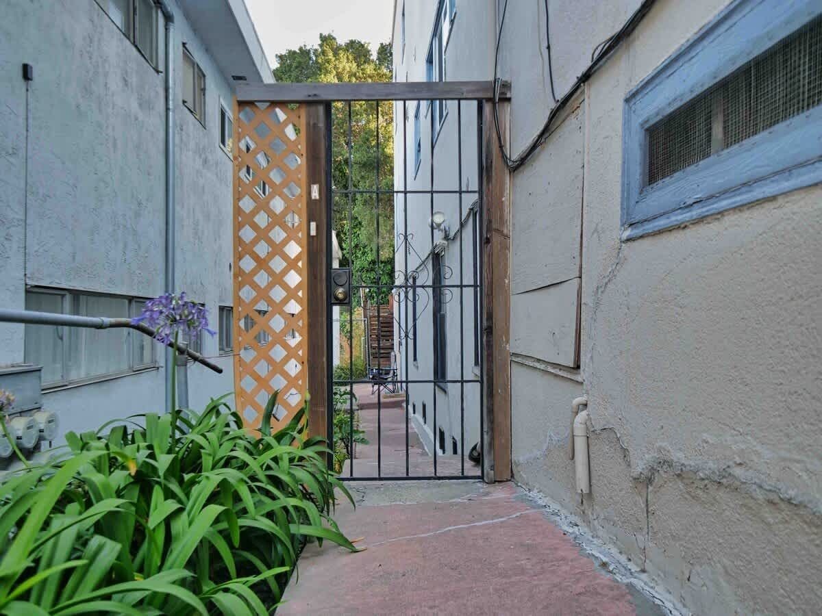 Un estrecho callejón con una entrada portonada, una reja de madera y un sendero que lleva a un edificio.