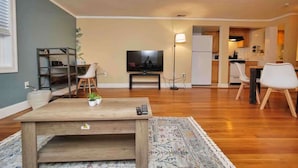 Una sala de estar con una mesa de centro de madera, un televisor y una cocina al fondo.