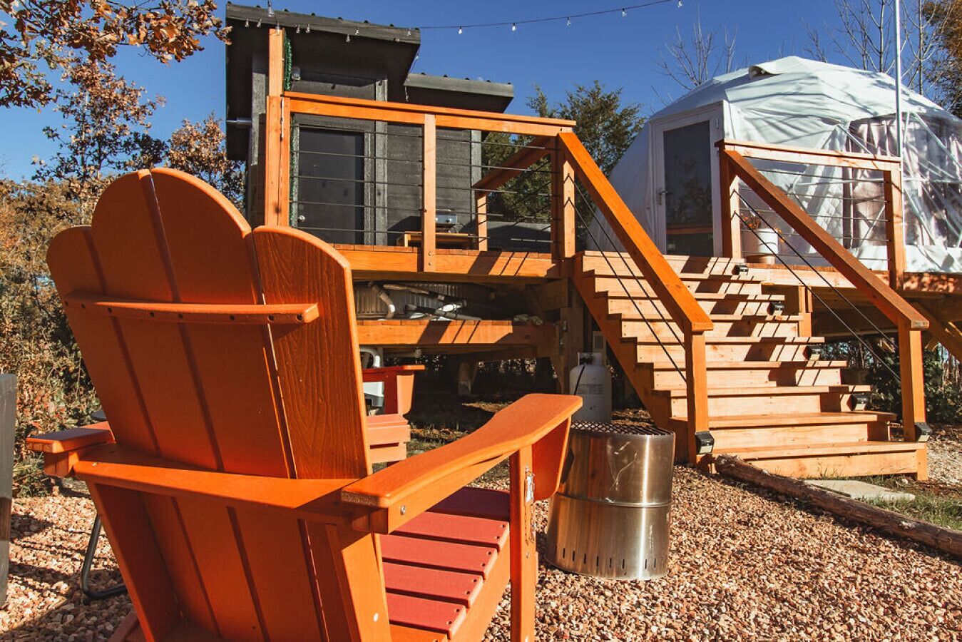 Eine Holzterrasse mit einem Stuhl, einem Metallmülleimer und einer Treppe, die zu einer überdachten Struktur führt.