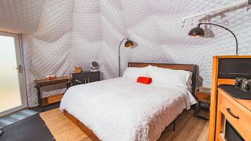 A cozy bedroom with a large bed, a wooden dresser, a nightstand, a lamp, and a quilted ceiling.
