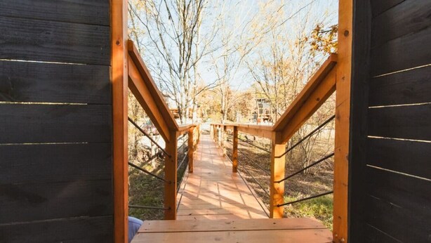 A wooden deck leading to a covered outdoor area with a view of trees and a clear sky. - The Tree House Dome at Selah Place (Athens)