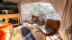 A tented accommodation with a kitchenette, two leather chairs, and a view of trees through a geometric window. - The Tree House Dome at Selah Place (Athens)