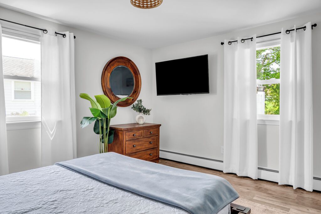 A bedroom with a bed, a dresser, a TV, and a window with curtains.