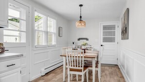 A kitchen with white cabinetry, a dining table with chairs, a hanging light fixture, and a door with a frosted glass panel. - Great Hammcock Getaway, cozy home, hot tub, fire pit, beaches nearby. (Old Saybrook)