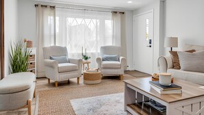 A modern living room with two armchairs, a sofa, a coffee table, and a large window with curtains. - Great Hammcock Getaway, cozy home, hot tub, fire pit, beaches nearby. (Old Saybrook)