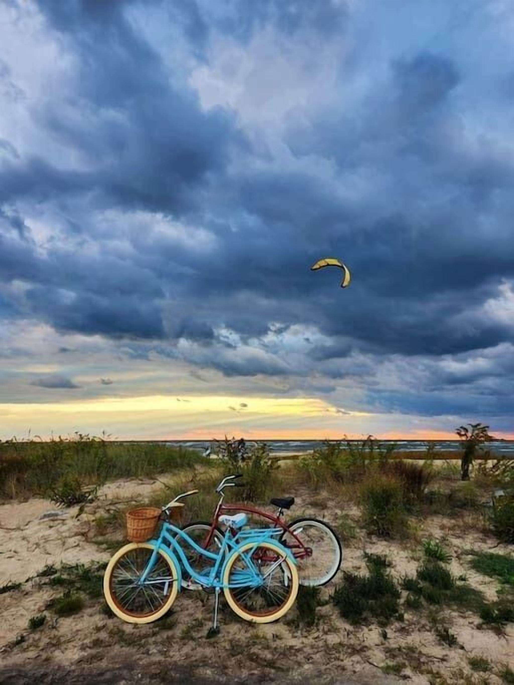Een fiets geparkeerd op een zanderig strand, met een bewolkte lucht en een verre horizon van de oceaan.