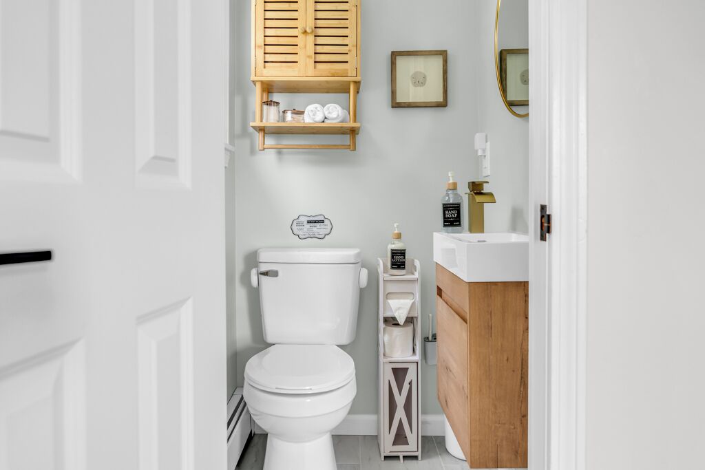 A modern bathroom with a white toilet, wooden shelves, a wooden vanity, and a framed picture on the wall.