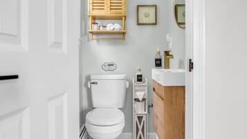 A modern bathroom with a white toilet, wooden shelves, a wooden vanity, and a framed picture on the wall.