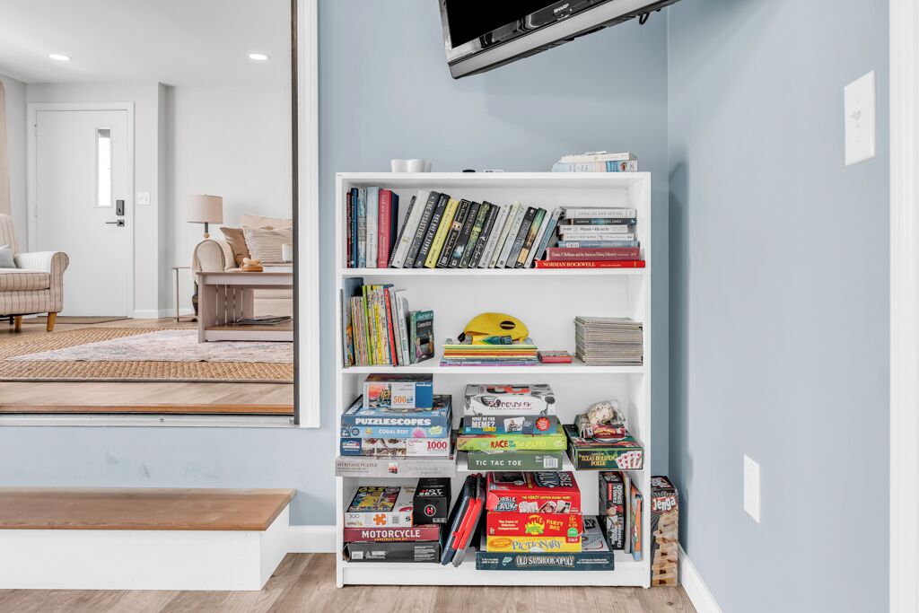 Un salon avec une bibliothèque remplie de livres et de jeux de société, un téléviseur fixé au mur et un canapé.