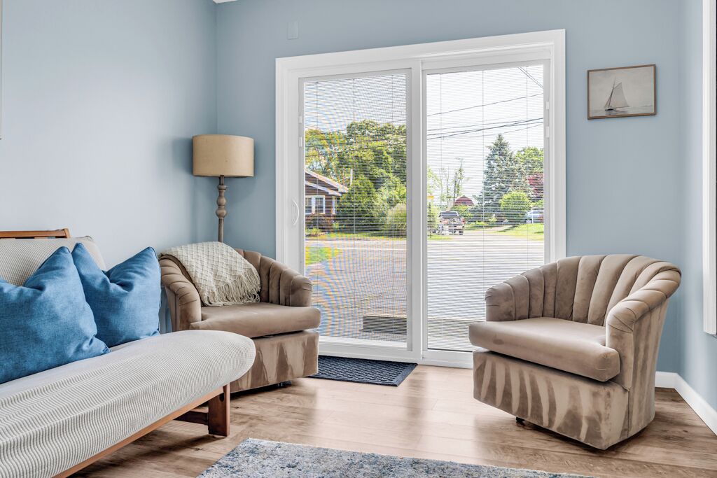 A living room with a sofa, two armchairs, a lamp, and a view through a glass door.