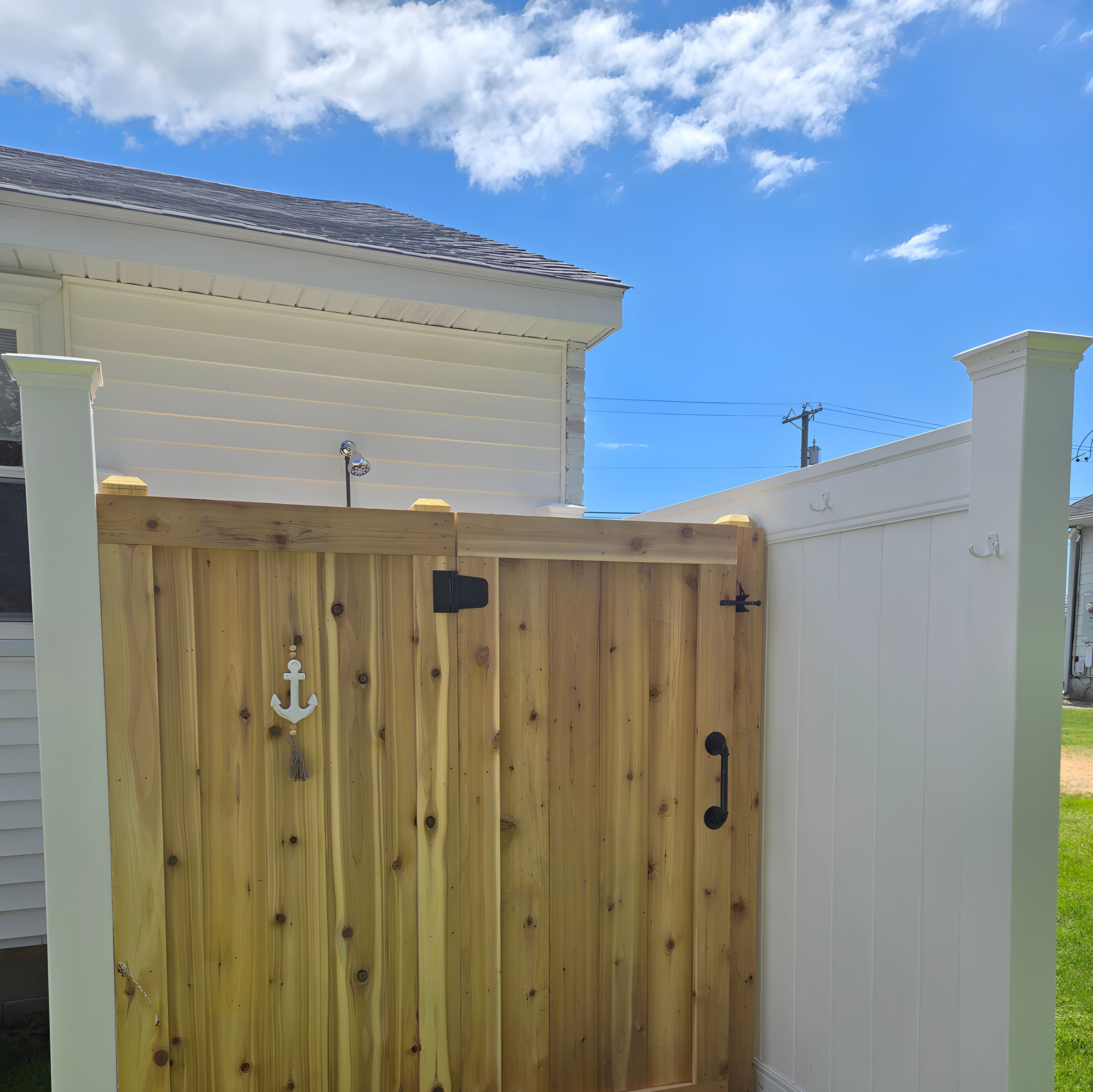 A wooden gate with an anchor decoration, a white picket fence, and a house with a light-colored exterior.