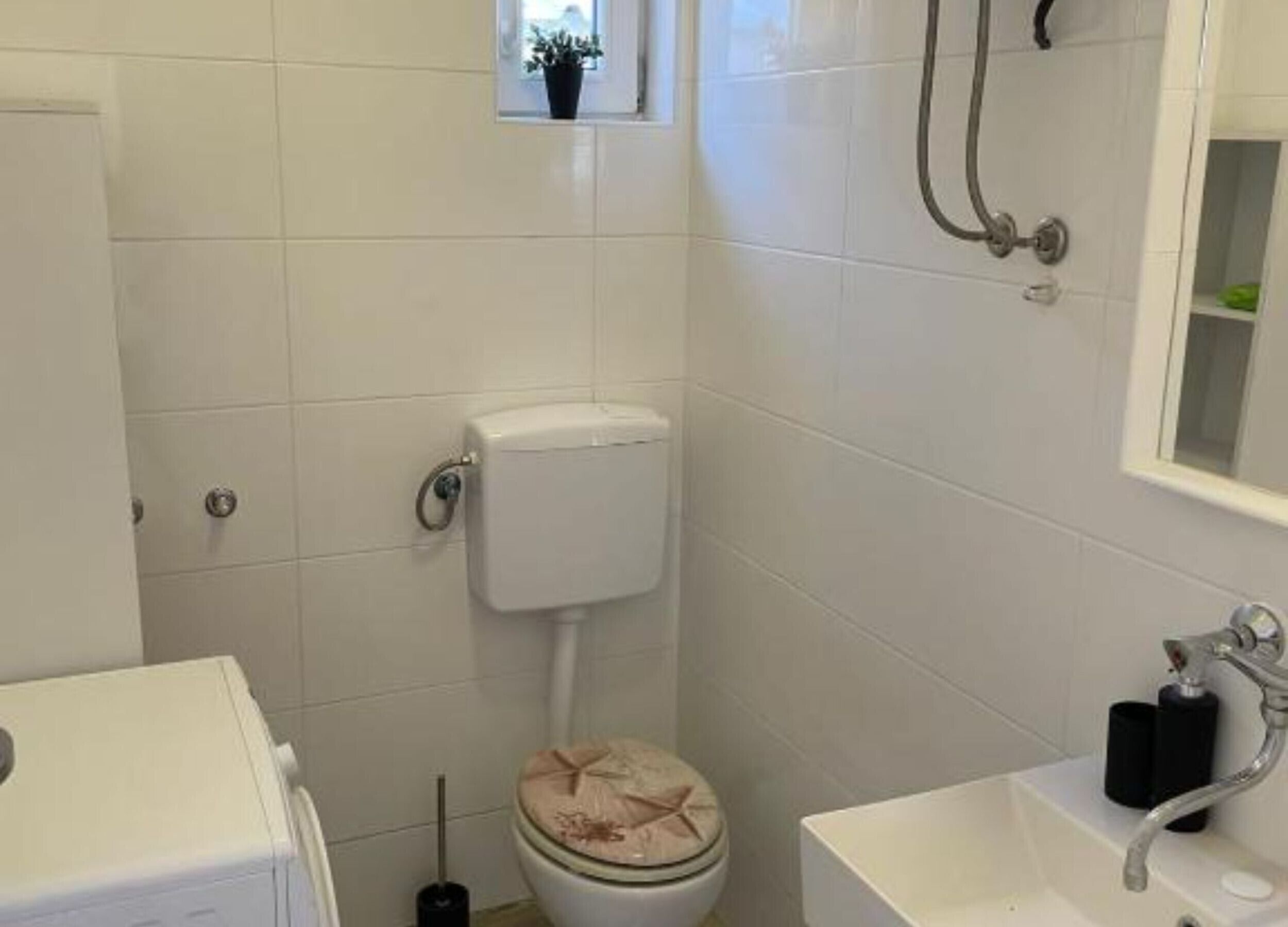 Pieni, siisti kylpyhuone, jossa on valkoiset laatat, wc-istuin, pesuallas ja suihku.