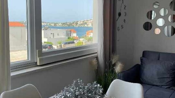 Una habitación con un ventanal que ofrece vistas a la costa, un sofá de color oscuro y una pared decorada con espejos redondos.